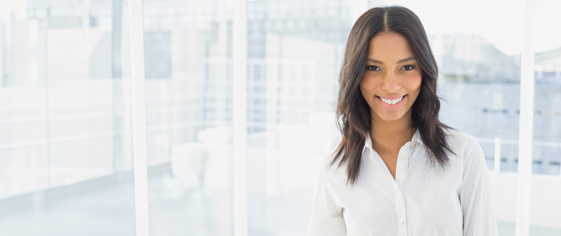 A smiling woman with short hair, wearing a white shirt and dark pants, stands against a blurred background with digital elements.