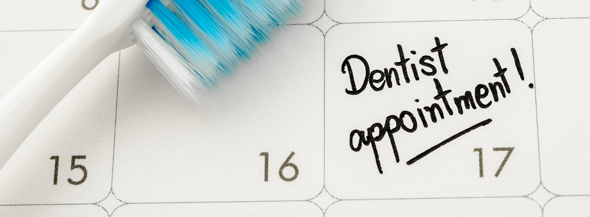 The image features a calendar with a toothbrush resting on top, displaying a playful message about dental appointments.