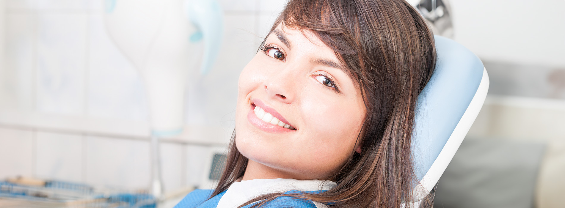 A smiling woman wearing glasses, sitting in an orthodontist s chair with braces on her teeth.