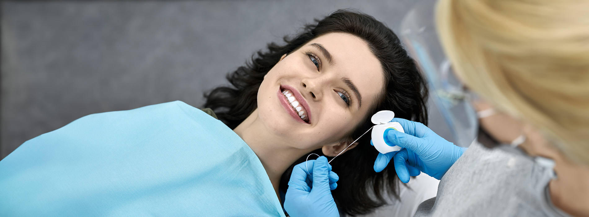 The image shows a woman lying down with her eyes closed, receiving dental care from another person who appears to be a dental professional, all set against a backdrop of a dental office environment.