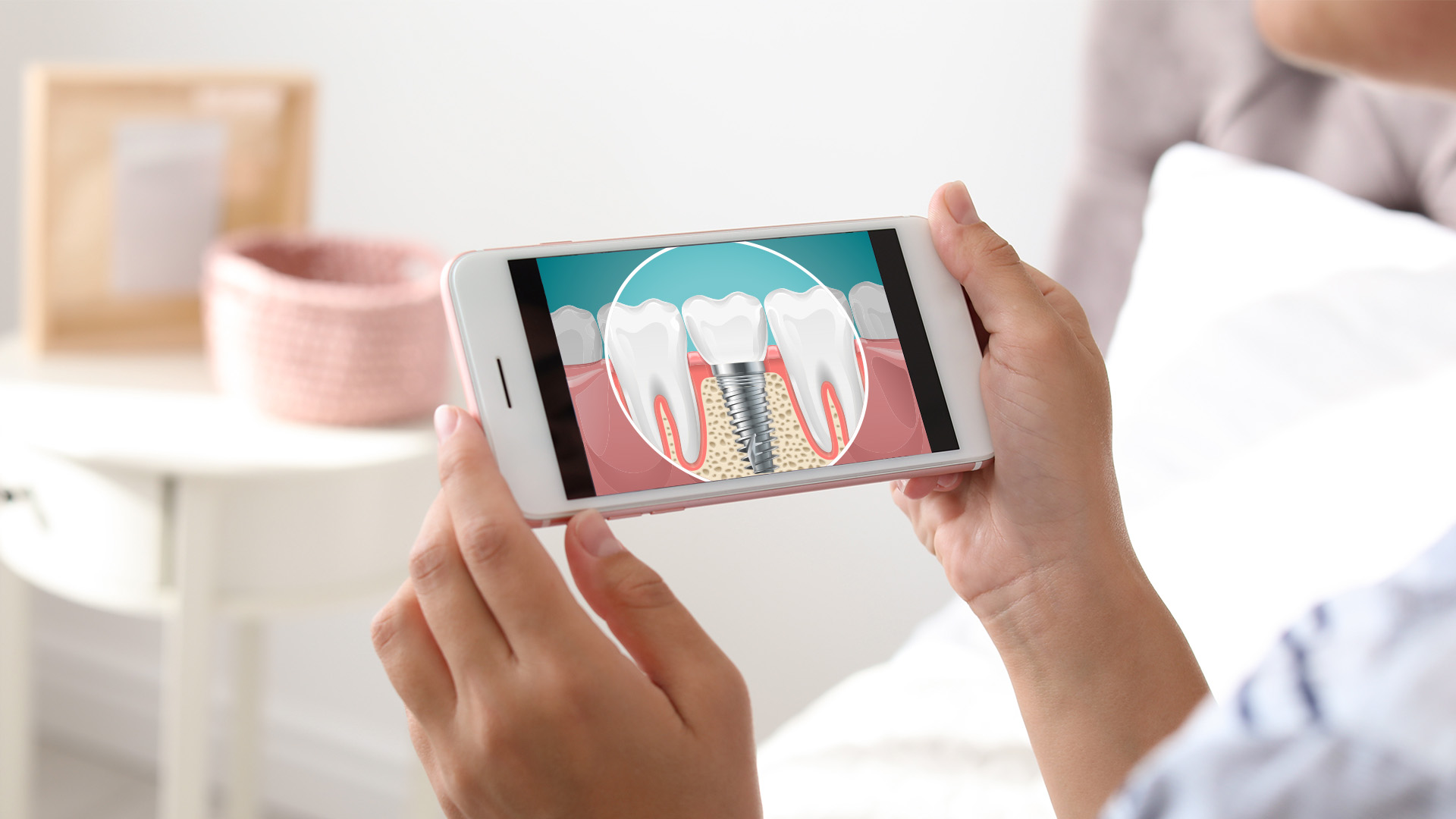 The image shows a person using a smartphone to view an illustration of a tooth with a cavity on a screen, held by two hands against a blurred background that appears to be a living room setting.