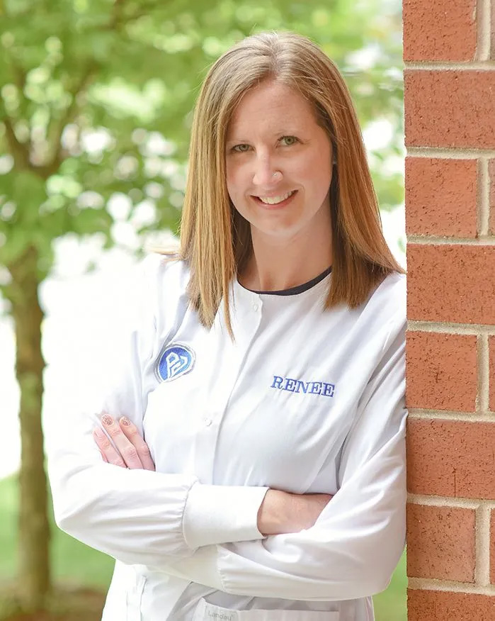 Woman standing against brick wall with hands on hips, smiling at camera.