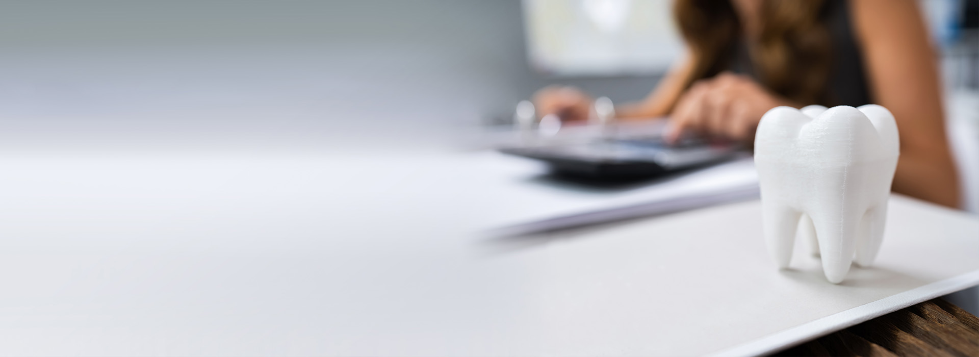 The image shows a person working at a desk with a computer monitor, keyboard, and mouse, accompanied by a small white toothbrush-shaped figurine on the table.