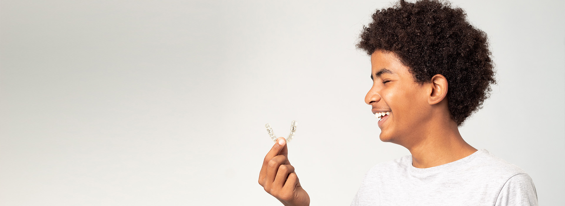 A young boy with curly hair holding a small object in his hand, smiling and looking upwards.