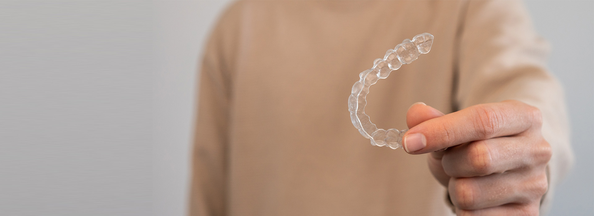A person s hand holding a transparent plastic object against a blurred background with a watermark-like design.