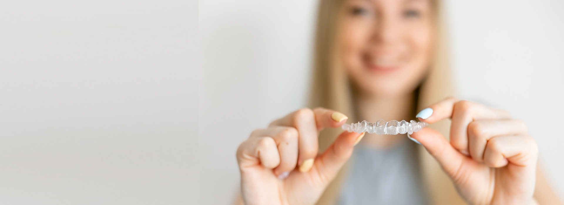 The image shows a person holding up a small object with their hand while facing the camera, with a white background highlighting the subject.