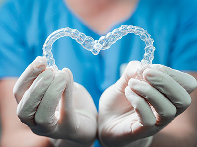 An individual s hand holding a clear heart-shaped object with a transparent texture, set against a blue background.