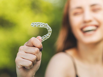 An individual holding up a clear plastic smiley keychain with teeth marks, smiling broadly at the camera.