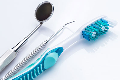 A photograph showing dental tools including toothbrushes with blue bristles and metal instruments on a white surface.