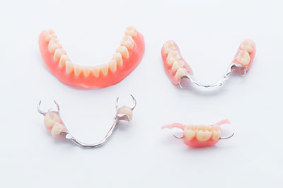 The image displays a collection of dentures with visible teeth, arranged on a white surface against a neutral background.