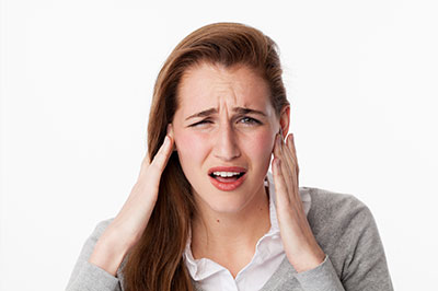 The image shows a young woman with her hand on her face, displaying an expression of shock or surprise, likely due to pain or discomfort.