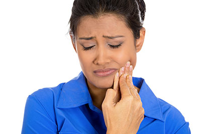 The image shows a woman with her eyes closed, holding her hand near her mouth, seemingly in distress or pain, against a plain background.