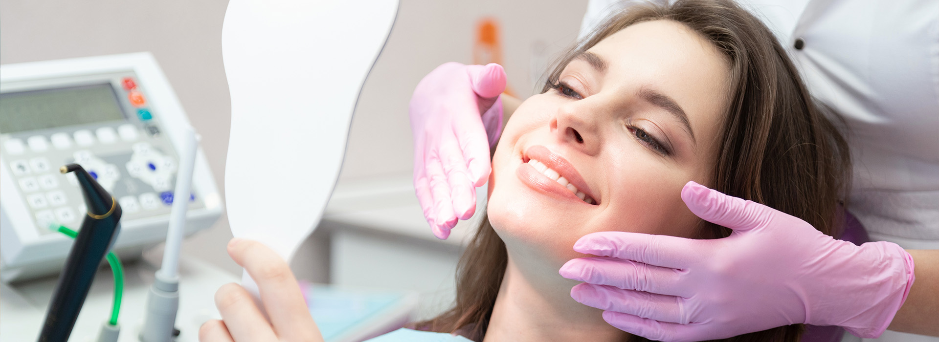 A woman receiving dental care while sitting in a dental chair, with a dentist attending to her, both wearing face masks.