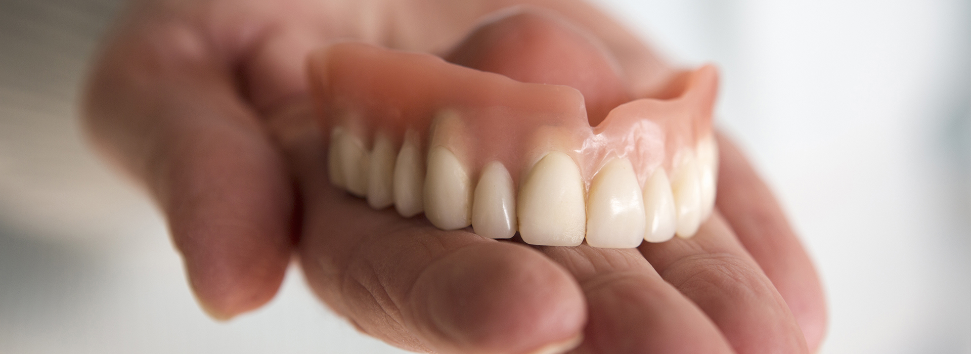 The image shows a person holding a set of artificial teeth.