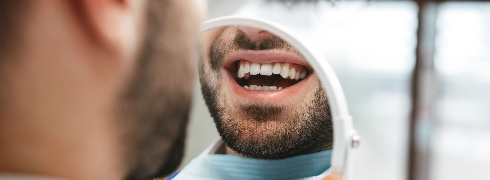 A man with a beard smiling at the camera while looking through a magnifying glass.