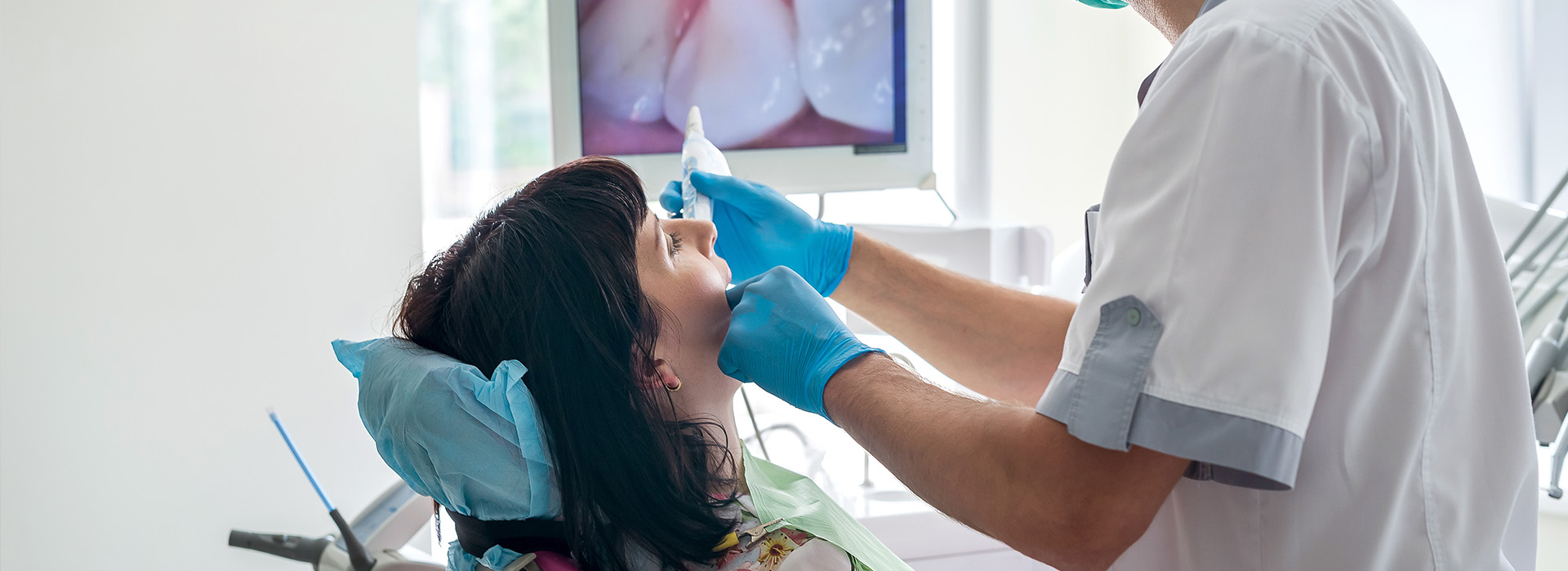 The image shows a dental hygienist performing a cleaning procedure on a patient s teeth, with the practitioner using a blue light tool.