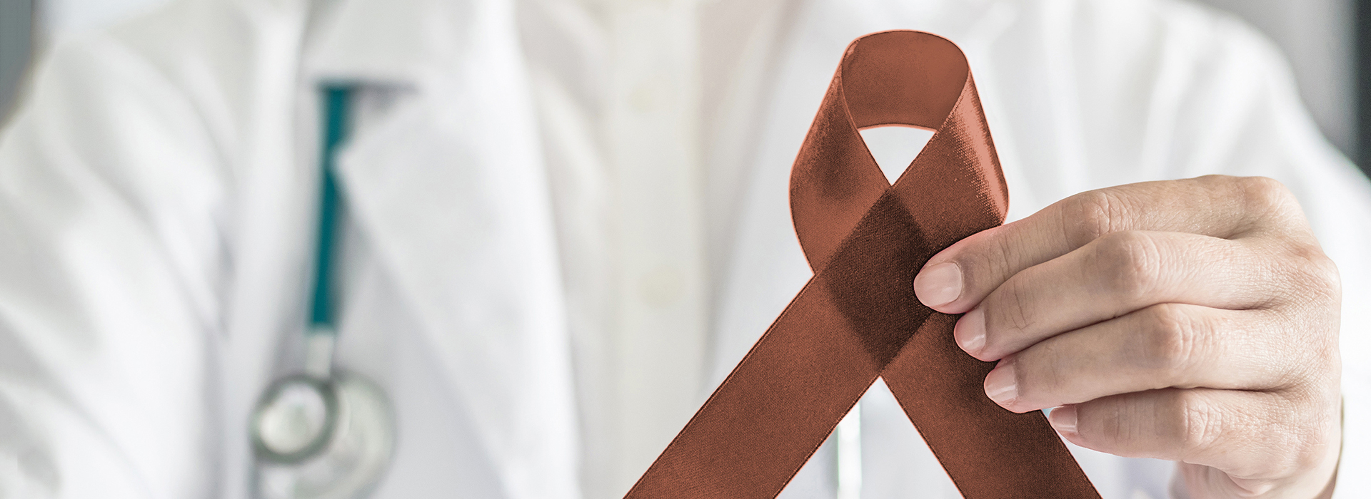 The image shows a healthcare professional holding up a red medical cross symbol with their left hand against a white background.