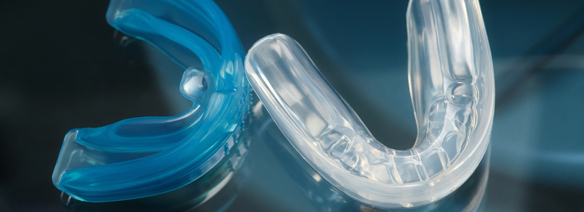 The image shows a close-up of a blue plastic object with a clear, translucent section in the center, possibly a part of a larger item, placed against a dark background that might suggest a water surface or a reflective material.