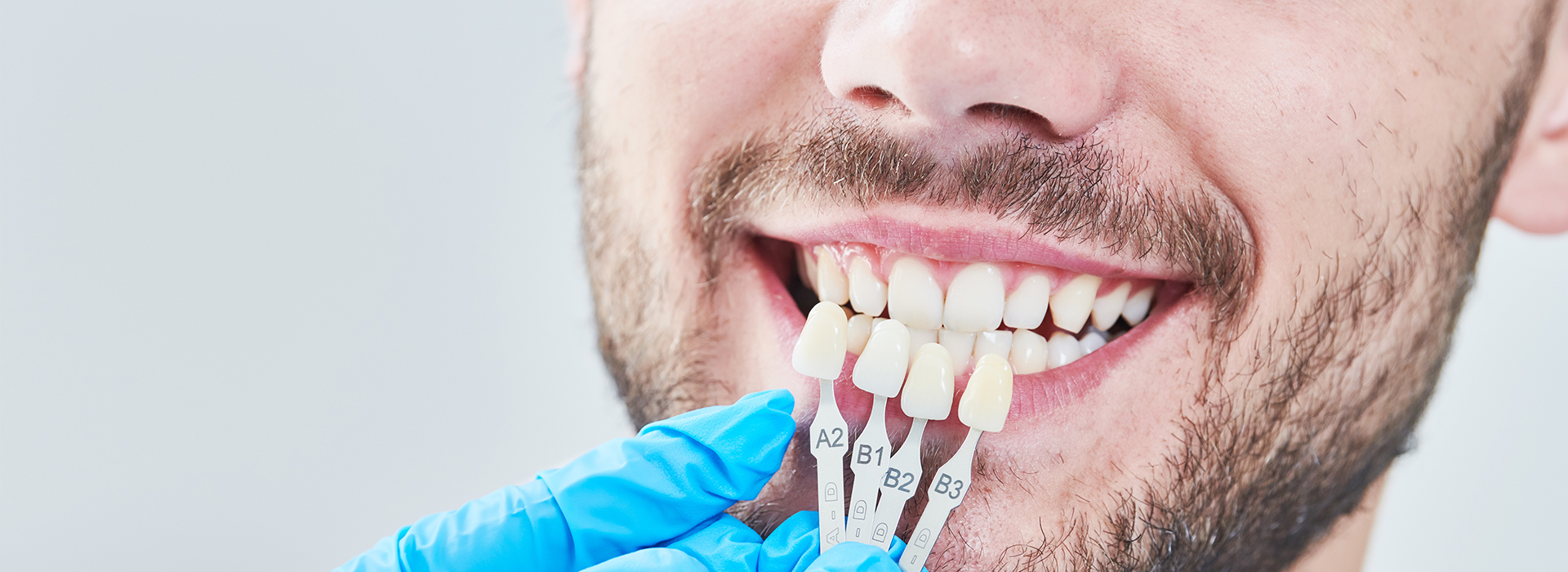A man with a big smile, possibly a dental professional, wearing blue gloves while holding a toothbrush near his mouth.