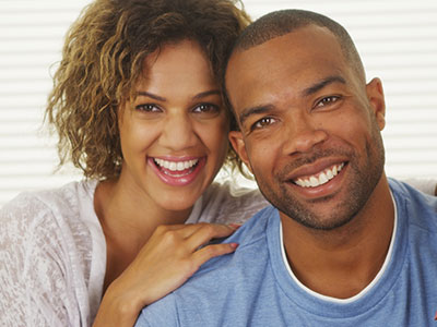 A man and woman are smiling at the camera  the man has short hair, the woman has long hair, and they both appear to be of African descent.