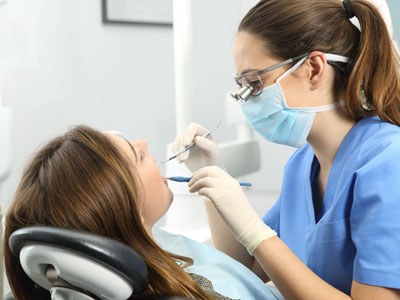 A dental hygienist is performing a cleaning procedure on a patient s teeth while wearing personal protective equipment  PPE .
