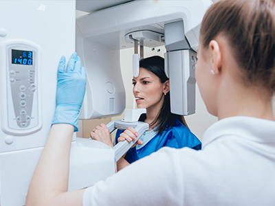 The image shows two individuals in a medical setting, with one person standing behind a large 3D scanner, and another person standing in front of it, looking at their reflection on the screen. They are both wearing surgical gowns and gloves, indicating a sterile environment.