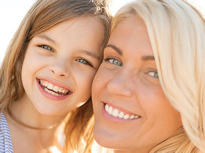 The image shows two individuals, an adult woman and a young girl, smiling at the camera with a warm and friendly demeanor, likely capturing a joyful family moment.