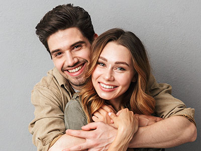 A young couple embracing with smiles, posing for a portrait against a neutral background.