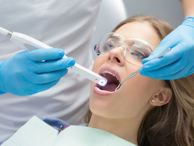A woman receiving dental treatment with a device that appears to be scanning her teeth while she sits in a dentist s chair, surrounded by dental professionals.