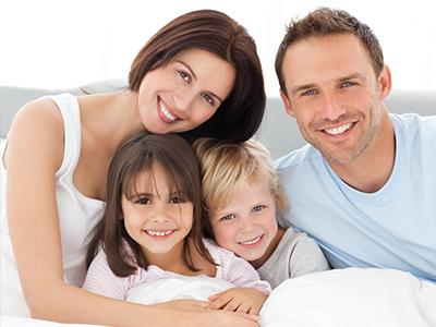 A family of four adults and two children posing together on a bed with smiles.