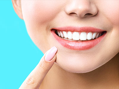 The image shows a close-up of a person s face with a bright smile, displaying white teeth and pink lips, against a blue background.